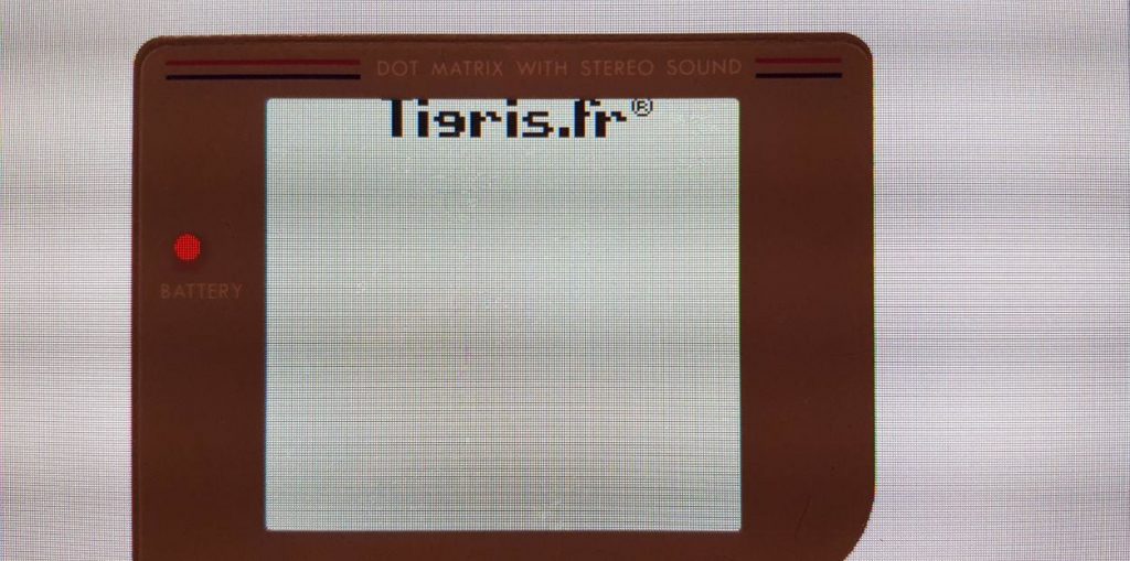 A poorly lit photo of a Game Boy screen cover on an LCD screen showing a Tigris logo scrolling down.