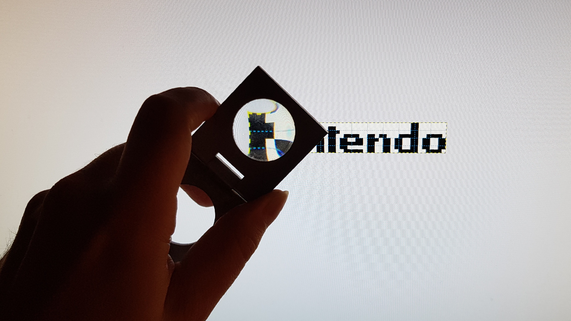 A photo of a magnifying glass held in front of the scaled up Nintendo logo on a computer screen.